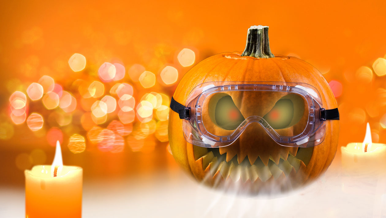 A carved pumpkin wearing goggles with 2 white burning candles next to it. 