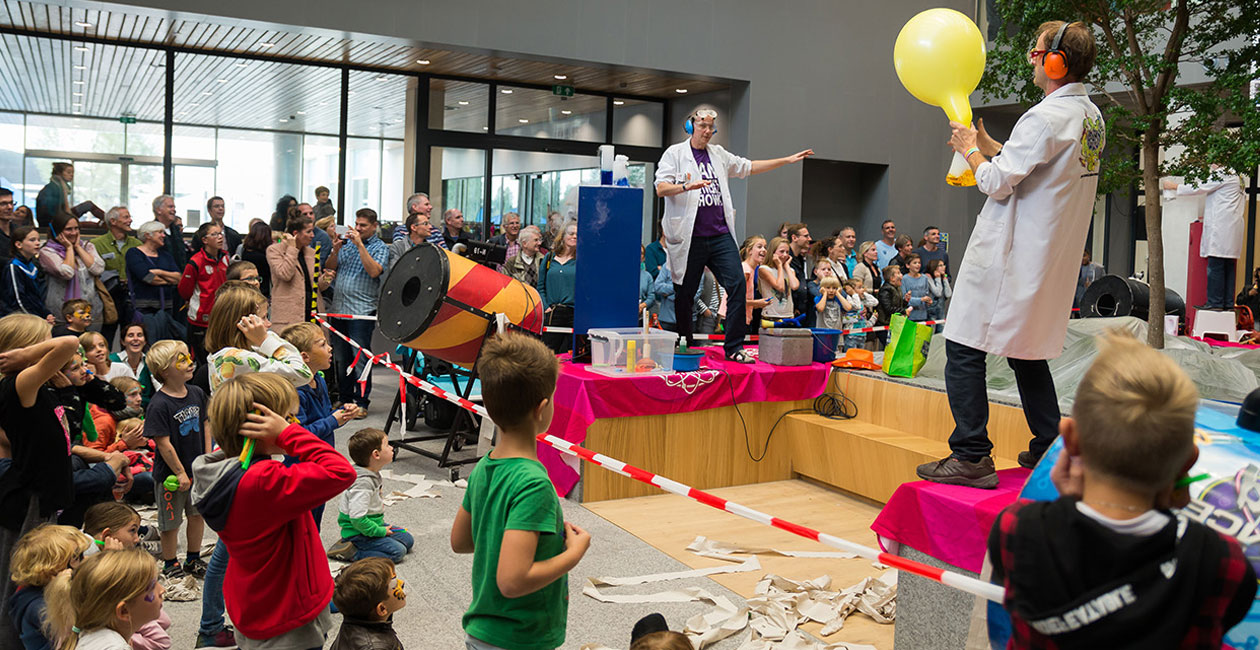 Mad scientist blowing up a balloon on stage in front of audience full of kids